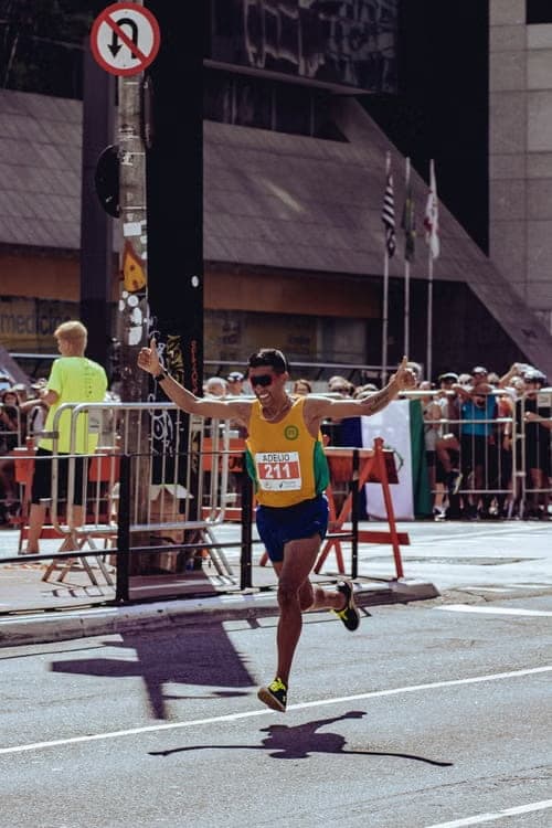 A runner crossing the finish line with both arms raised beneath the finish gantry