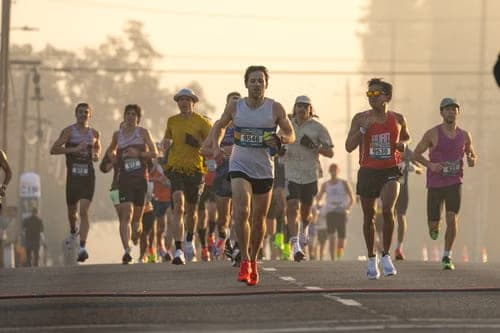 A dense pack of runners moving off the start line, race bibs visible